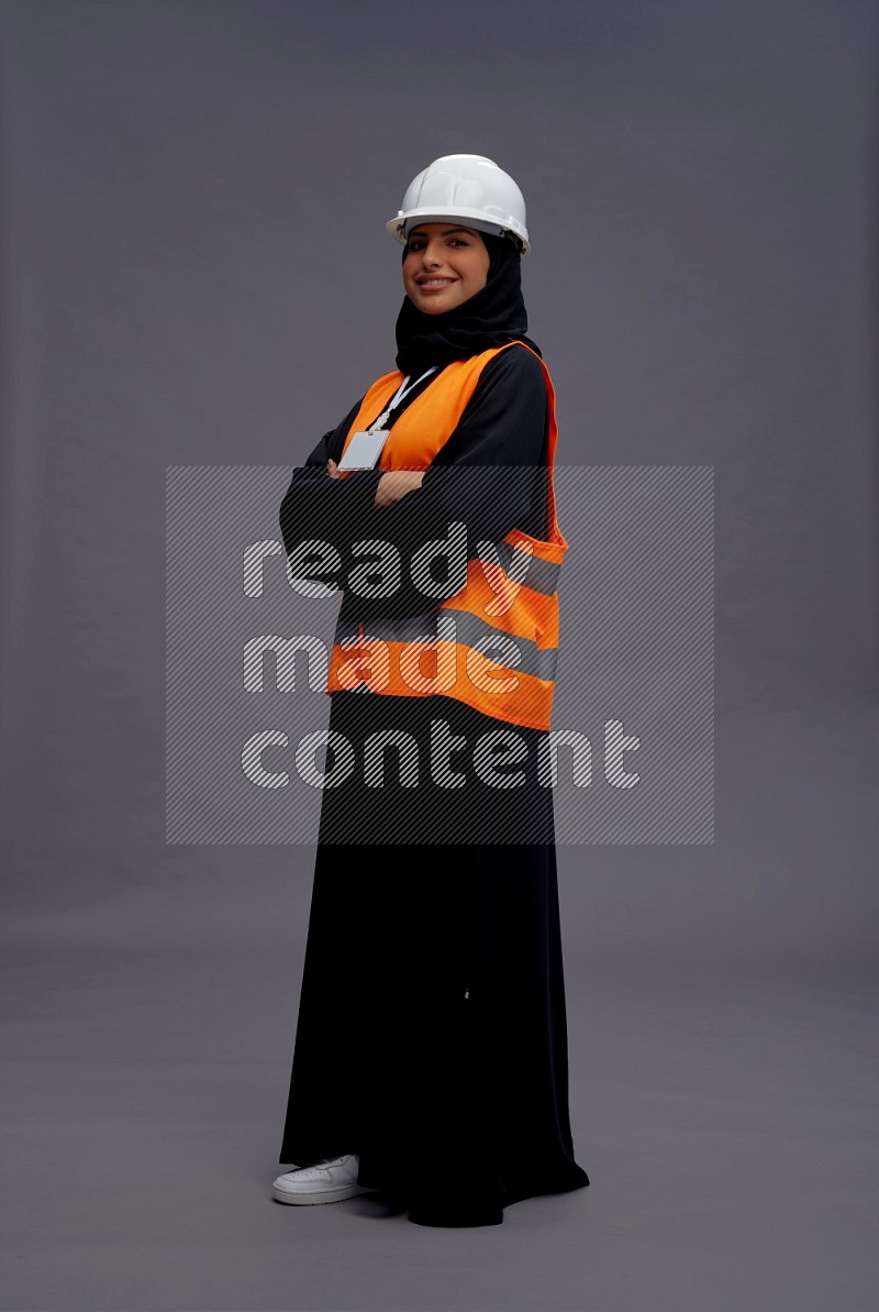 Saudi woman wearing Abaya with engineer vest with neck strap employee badge standing with crossed arms on gray background