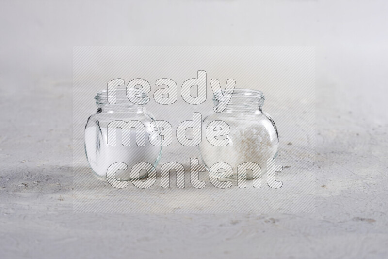 2 glass jars one is filled with table salt and the other with coarse sea salt on white background