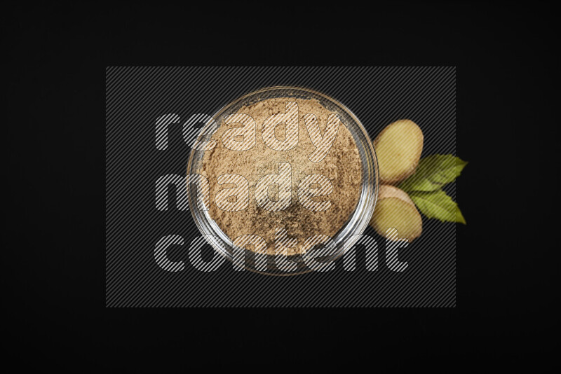 A glass bowl full of ground ginger powder on black background