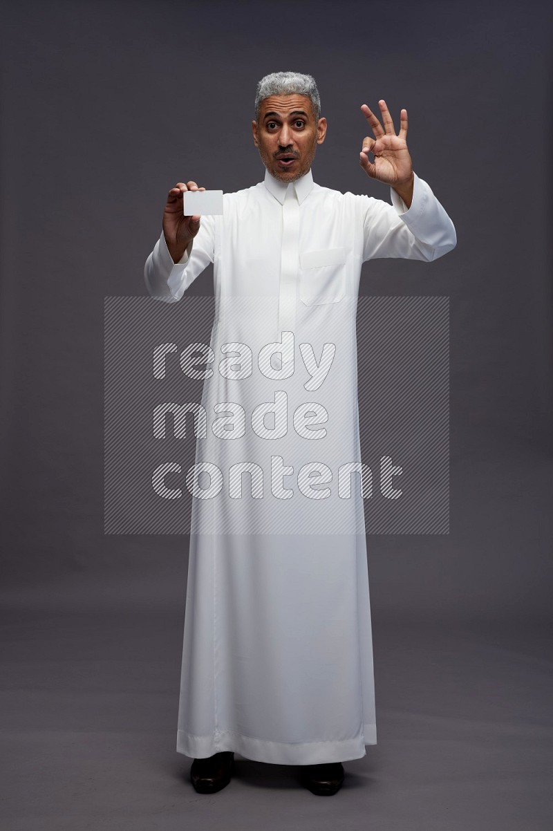 Saudi man wearing thob standing holding ATM card on gray background