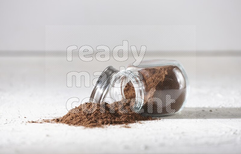 A flipped glass spice jar full of cloves powder and powder came out of it on textured white flooring