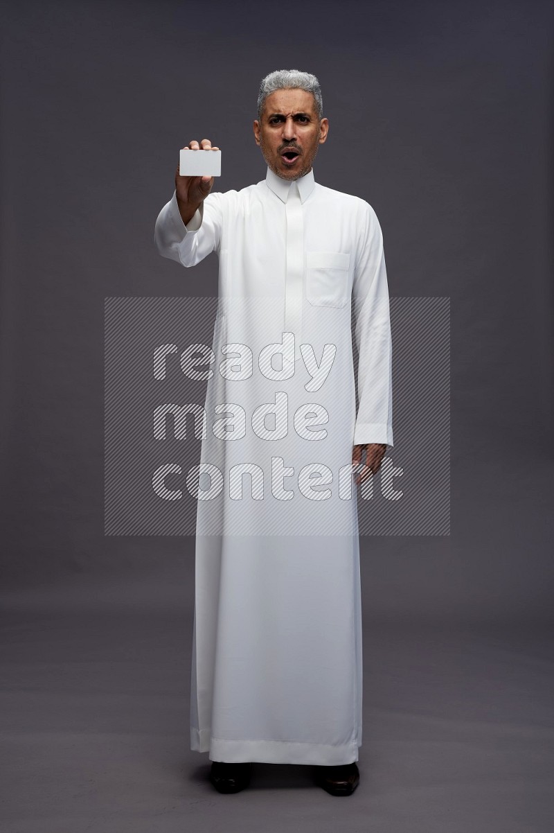 Saudi man wearing thob standing holding ATM card on gray background