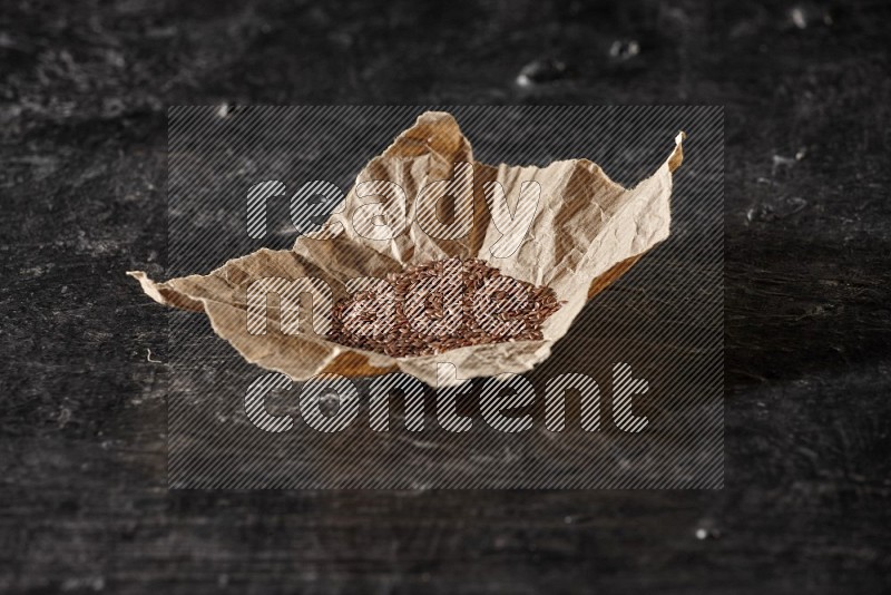A crumpled piece of paper full of flax on a textured black flooring in different angles