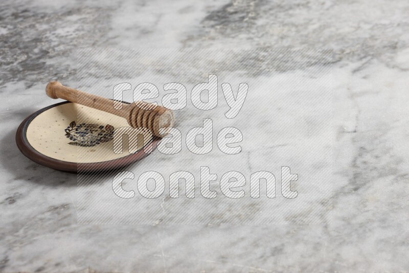 طبق فخاري مزخرف مع ملعقة عسل خشبية بداخله على خلفية من الرخام الرمادي