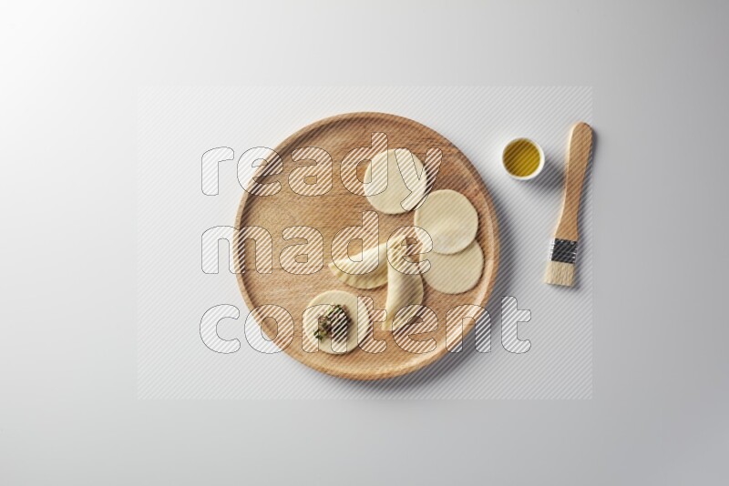 two closed sambosas and one open sambosa filled with meat while oil with oil brush aside in a wooden dish on a white background