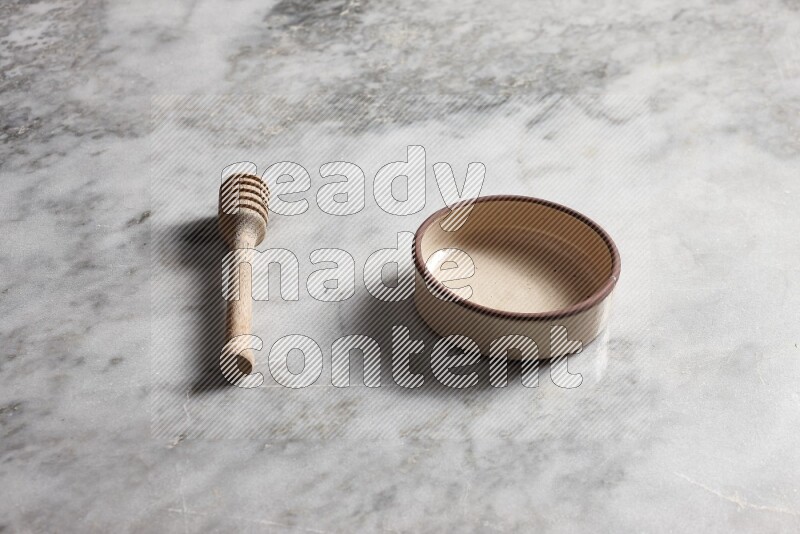 Beige pottery oven bowl with wooden honey dipper on the side on grey marble background
