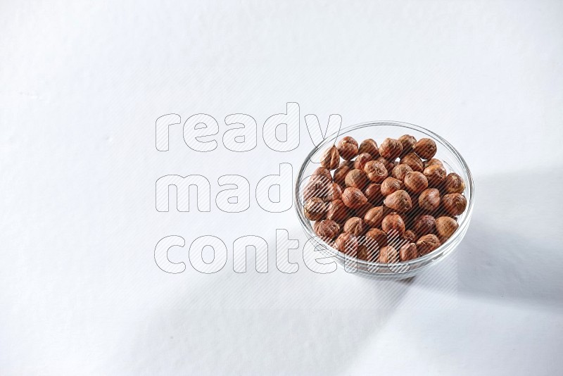 A glass bowl full of peeled hazelnuts on a white background in different angles