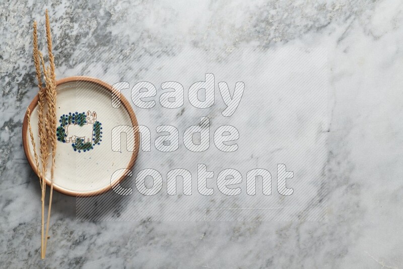 Wheat stalks on decorative pottery plate on grey marble background