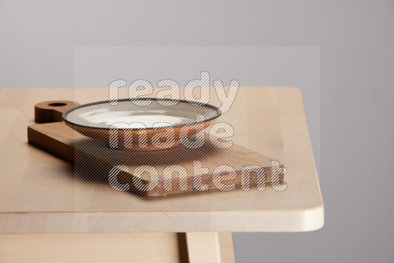 multi-colored pottery Plate placed on a  wooden rectangular cutting board on the edge of wooden table