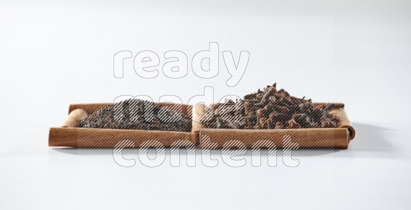 مربعان من أعواد القرفة ممتلئان بالشاي الأسود وحبوب القرنفل علي خلفية بيضاء