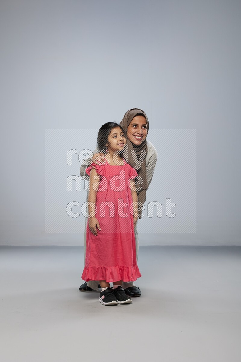 A girl and her mother interacting with the camera on gray background
