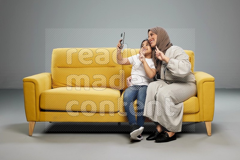 A girl sitting taking selfie with her mother on gray background