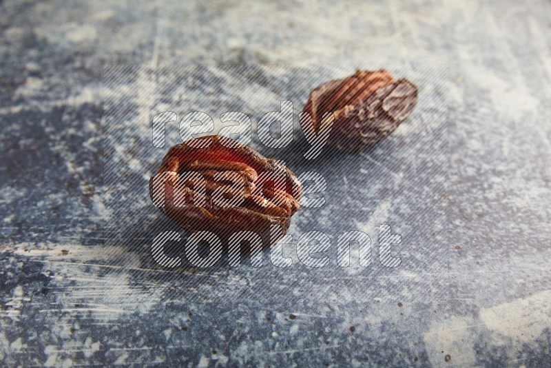 two pecan stuffed madjoul dates on a rustic blue background