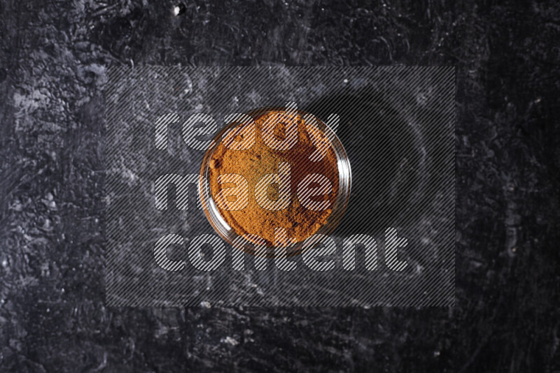 A glass bowl full of ground paprika powder on black background