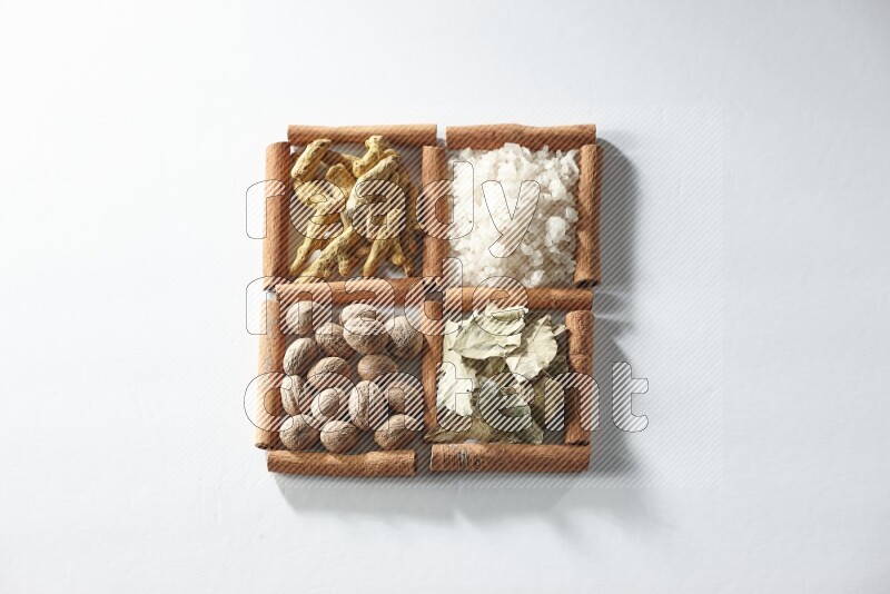 4 مربعات من أعواد القرفة ممتلئة بالملح وورق الغار وجوزة الطيب والكركم على أرضية بيضاء