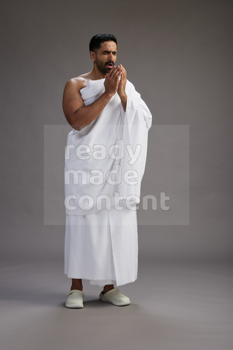 A man wearing Ehram standing showing how to sneeze on gray background