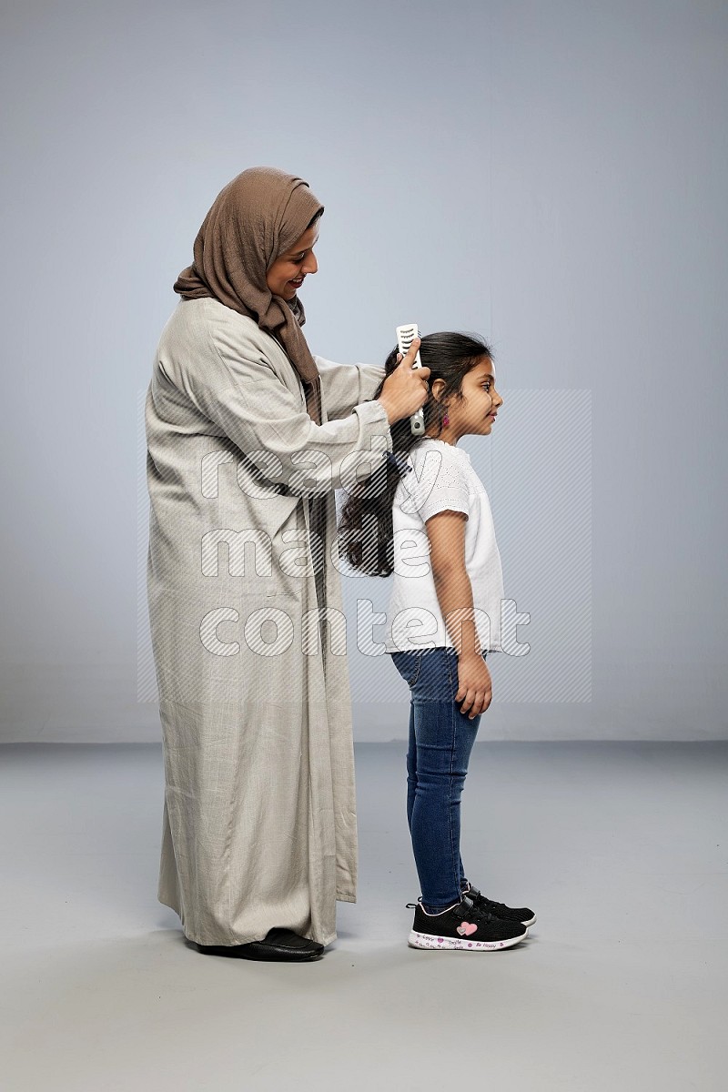 Mom standing styling hair for her daughter on gray background