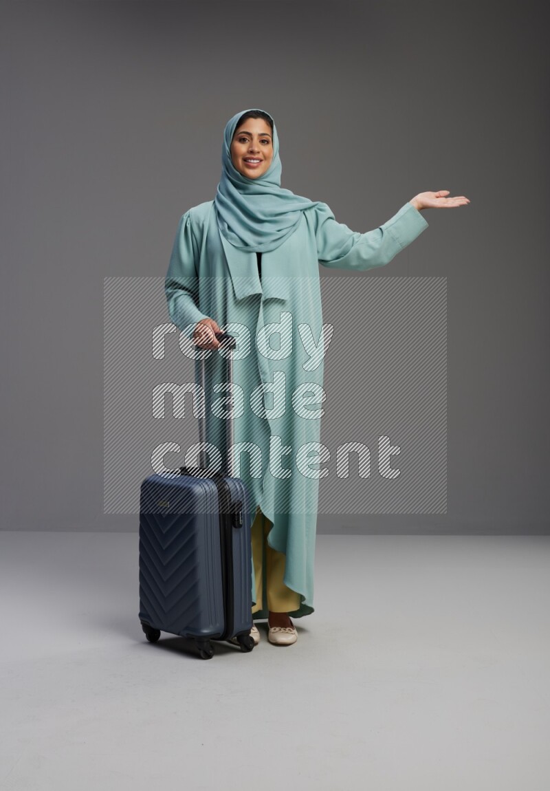Saudi Woman wearing Abaya standing holding Travel bag on Gray background
