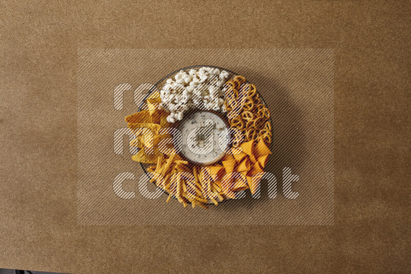 Assorted snacks on a pottery plate with a dipping on brown background
