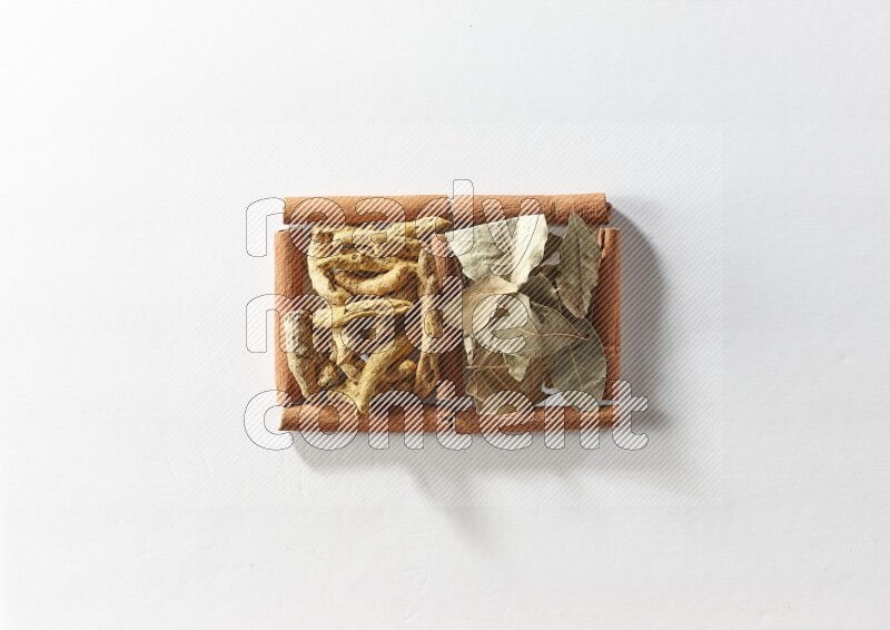 مربعان من أعواد القرفة ممتلئان بأصابع الكركم وأوراق الغار علي خلفية بيضاء