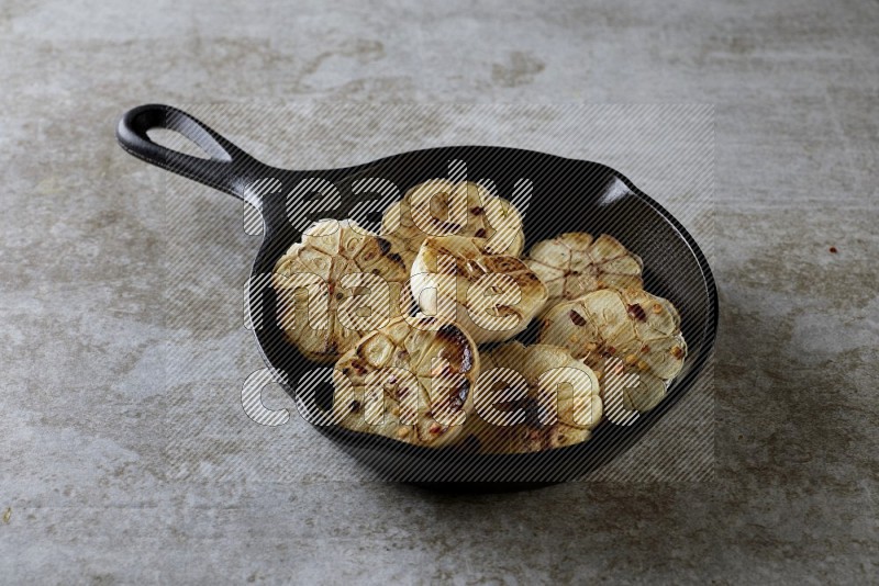 half's roasted garlic in a black pan on a grey textured countertop