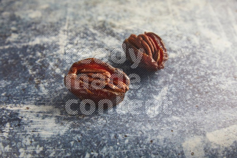 two pecan stuffed madjoul dates on a rustic blue background