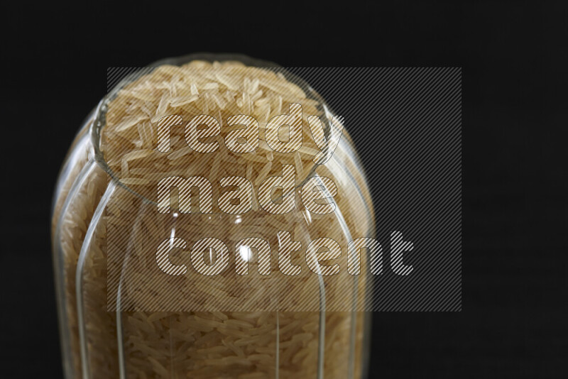 Basmati golden rice in a glass jar on black background