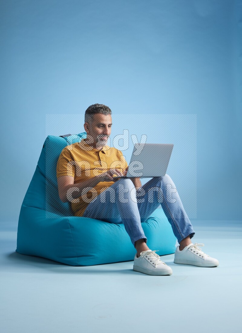 A man sitting on a blue beanbag and working on laptop