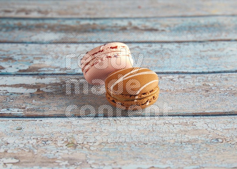 45º Shot of of two assorted Brown Irish Cream, and pink orange blossom  macarons on light blue background