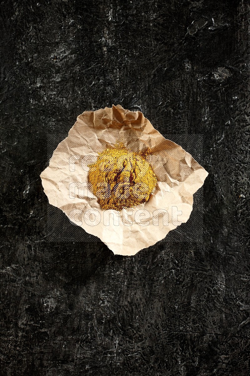 Turmeric powder in a crumpled piece of paper on textured black flooring