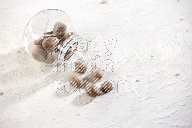 A glass spice jar full of nutmeg flipped and the seeds came out on a textured white flooring in different angles