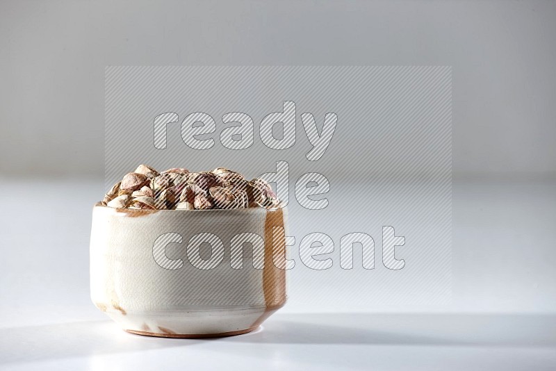 A beige ceramic bowl full of peeled pistachios on a white background in different angles