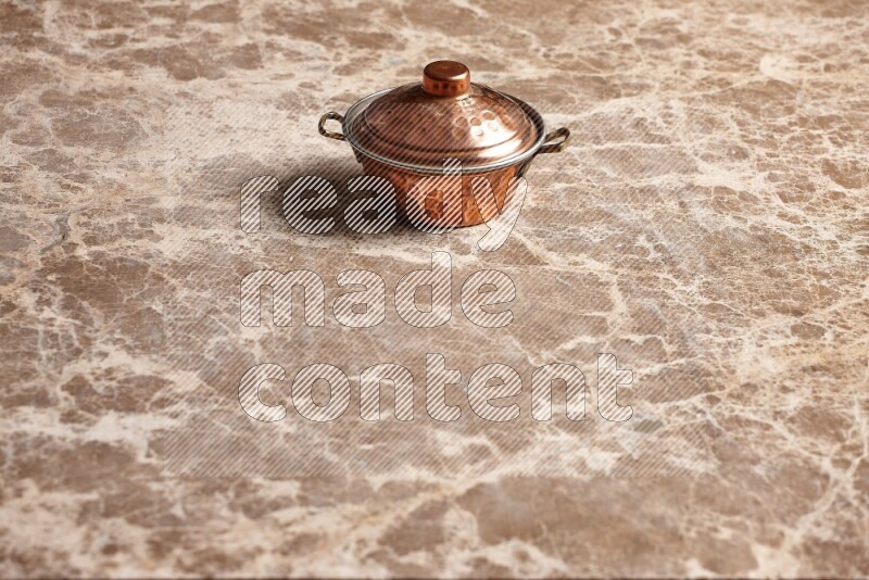 A small copper pot on beige marble background