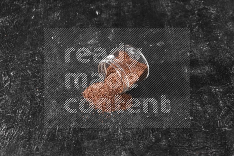 A glass jar full of garden cress seeds flipped and seeds spread out on a textured black flooring