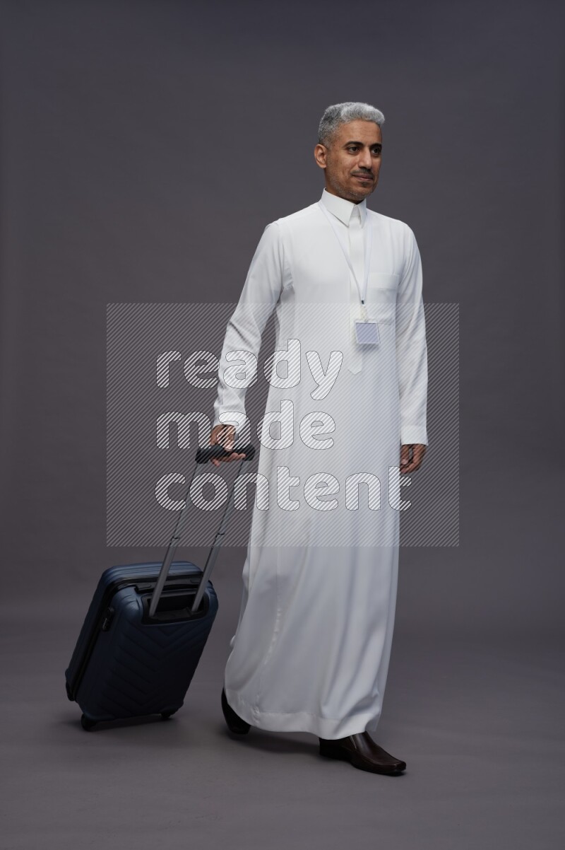 Saudi man wearing thob with neck strap employee badge standing holding bag on gray background
