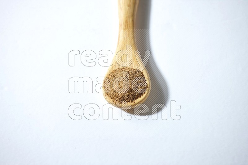A wooden spoon full of cumin powder on a white flooring