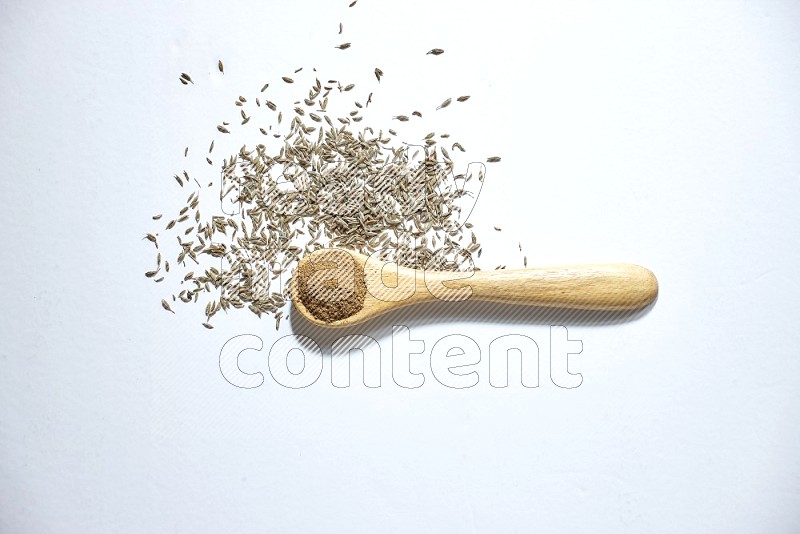 A wooden spoon full of cumin powder and cumin seeds beside it on white flooring