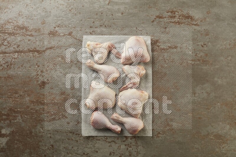 Mixed fresh chicken pieces on a parchment paper direct on a textured rustic background