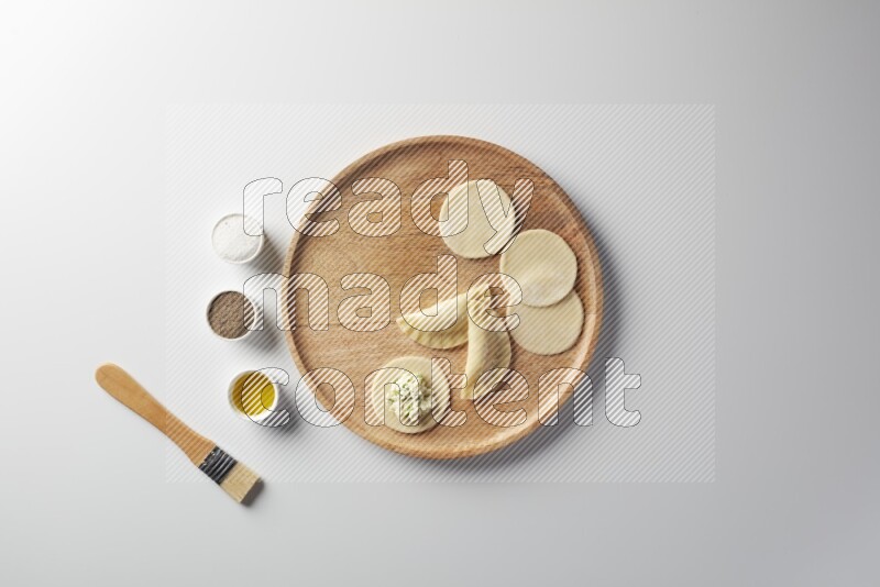 two closed sambosas and one open sambosa filled with cheese while salt, black pepper and oil with oil brush aside in a wooden dish on a white background