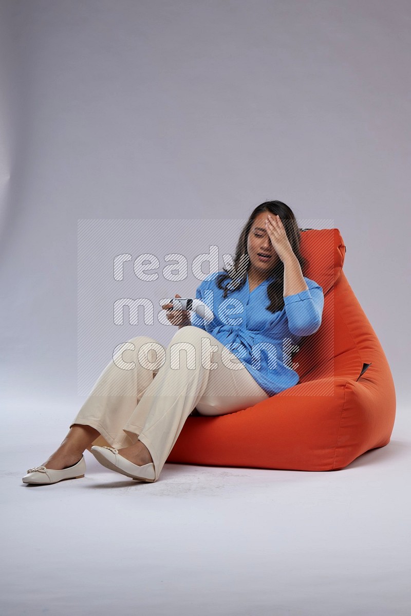 A woman sitting on an orange beanbag and gaming with joystick