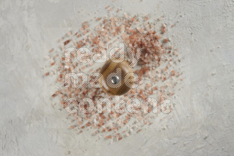 A wooden grinder standing upright and surrounded by coarse pink himalayan salt on white background