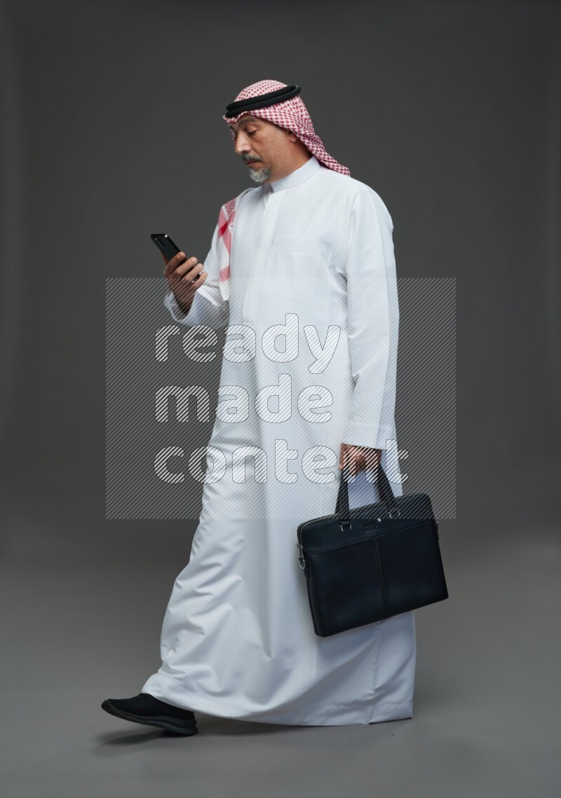 Saudi man with shomag Standing holding bag and phone on gray background