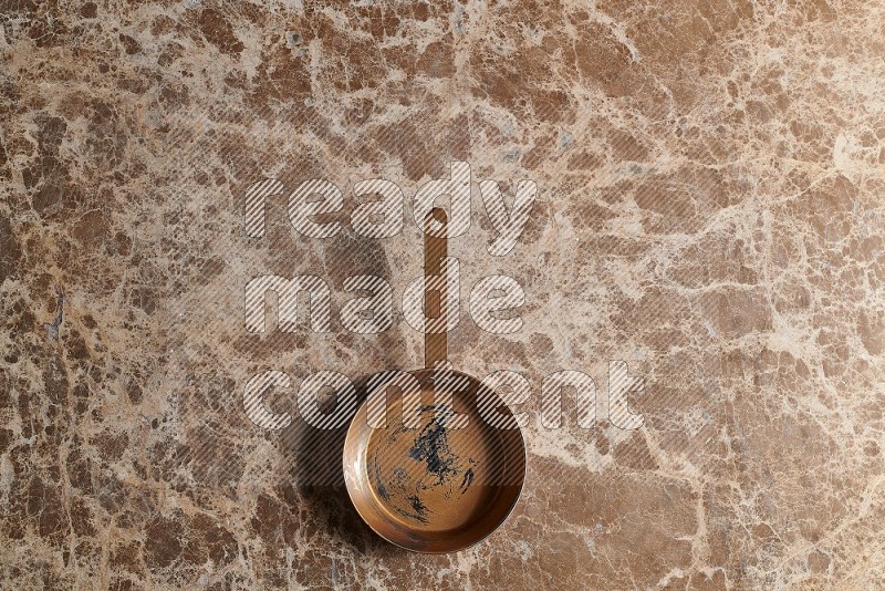 Top View Shot Of A Small Copper pan On beige Marble Flooring