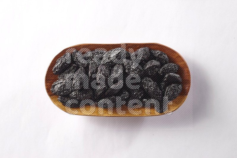 Dried plums in a wooden plate on white background