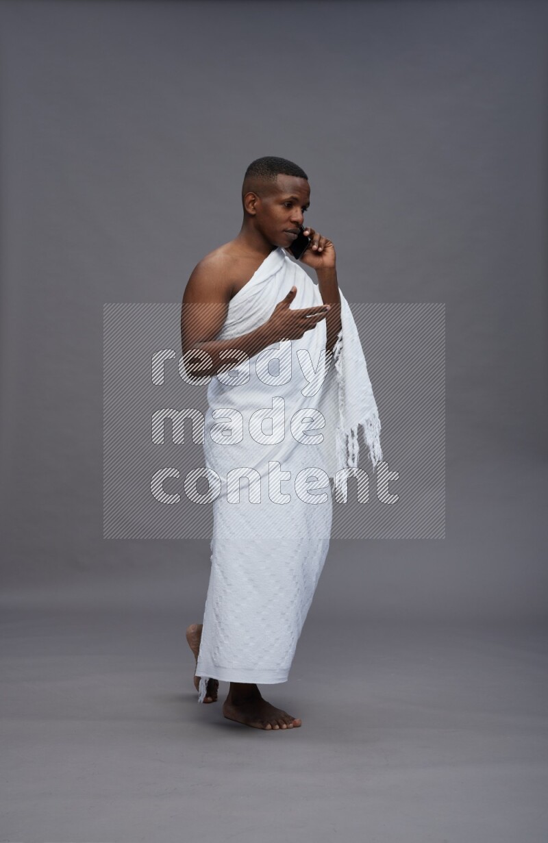 A man wearing Ehram Standing talking on phone on gray background