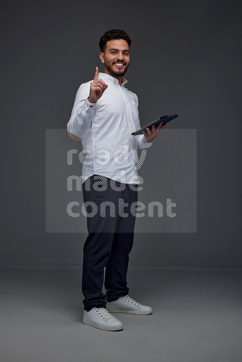 A man wearing smart casual standing and using his tablet and making multi hand gestures eye level on a gray background