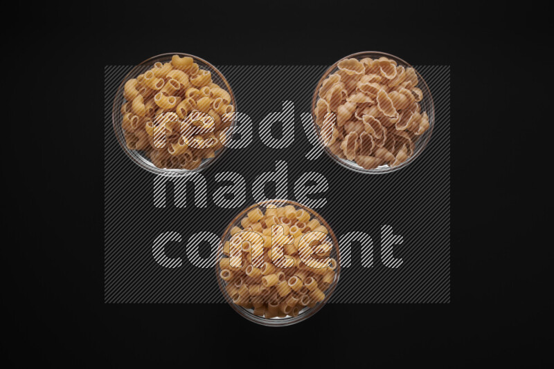Different pasta types in glass bowls on black background