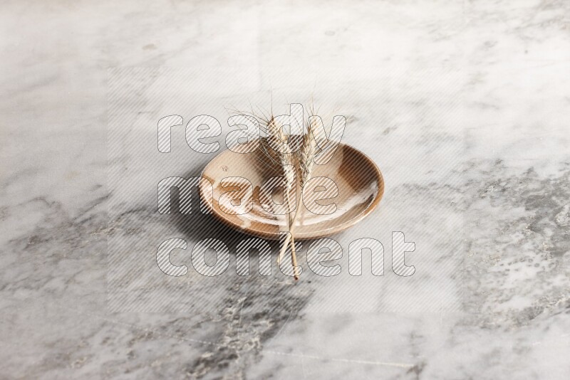 Wheat stalks on multicolored pottery plate on grey marble background