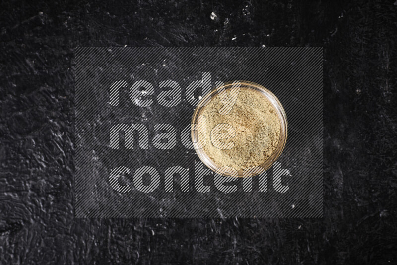 A glass jar full of ground ginger powder on black background