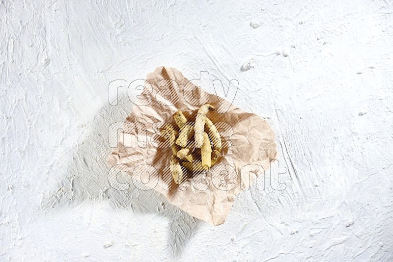 Dried turmeric whole fingers in a crumpled piece of paper on textured white flooring